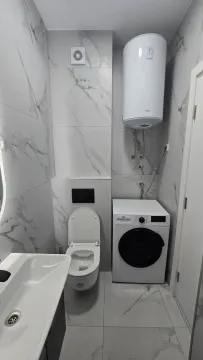 Moderno opremljeno kupatilo sa bijelim mermernim pločicama, wc šoljom, umivaonikom i veš mašinom. - image 13