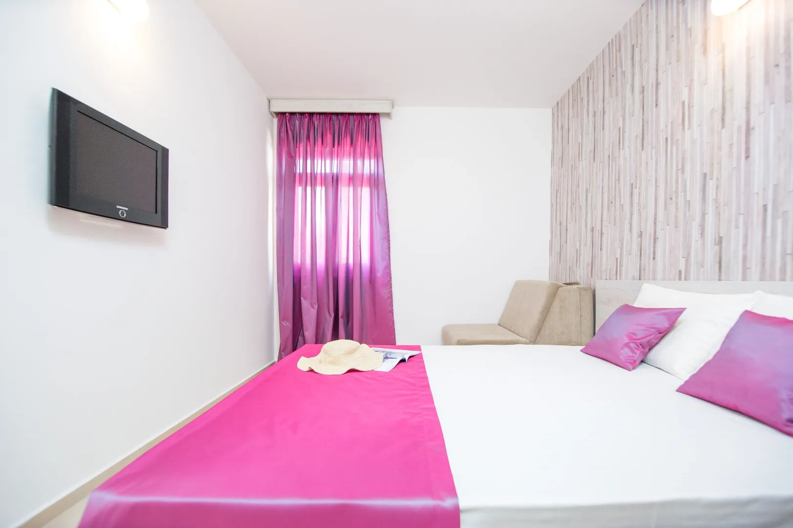 Bright bedroom with a double bed, TV, and purple details.
