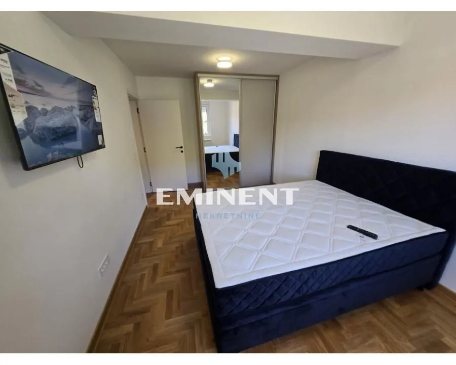 Furnished bedroom with a double bed, wardrobe, and wall-mounted television.
