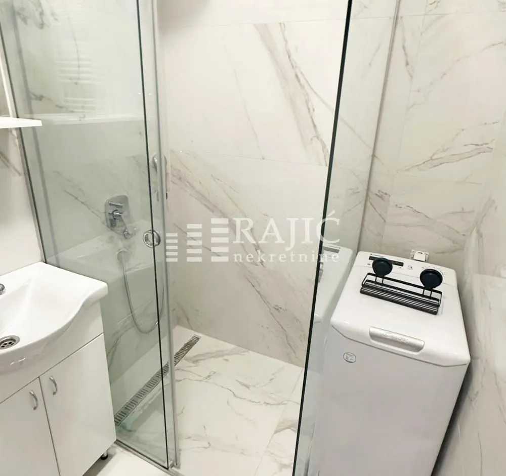 Modern bathroom with a shower cabin, washbasin, and washing machine.