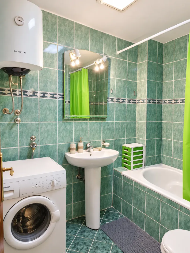 Small bathroom with green tiles, washbasin, bathtub, and washing machine.