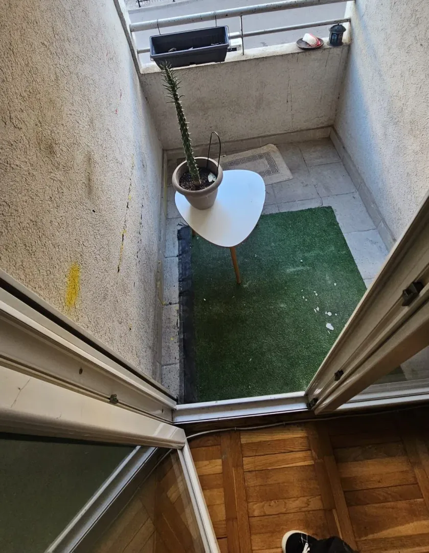 Manji namješten balkon sa vještačkom travom i stolom sa saksijom.