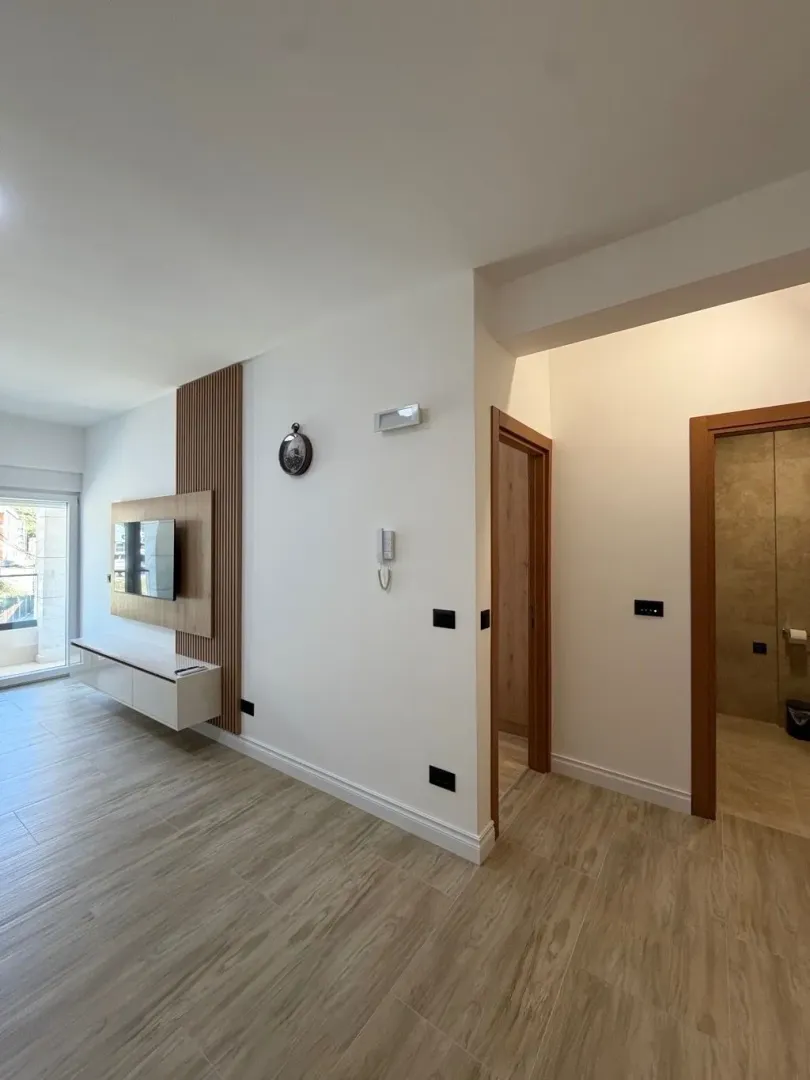 Living room with a wooden accent wall and TV, showing doors to the hallway and bathroom.