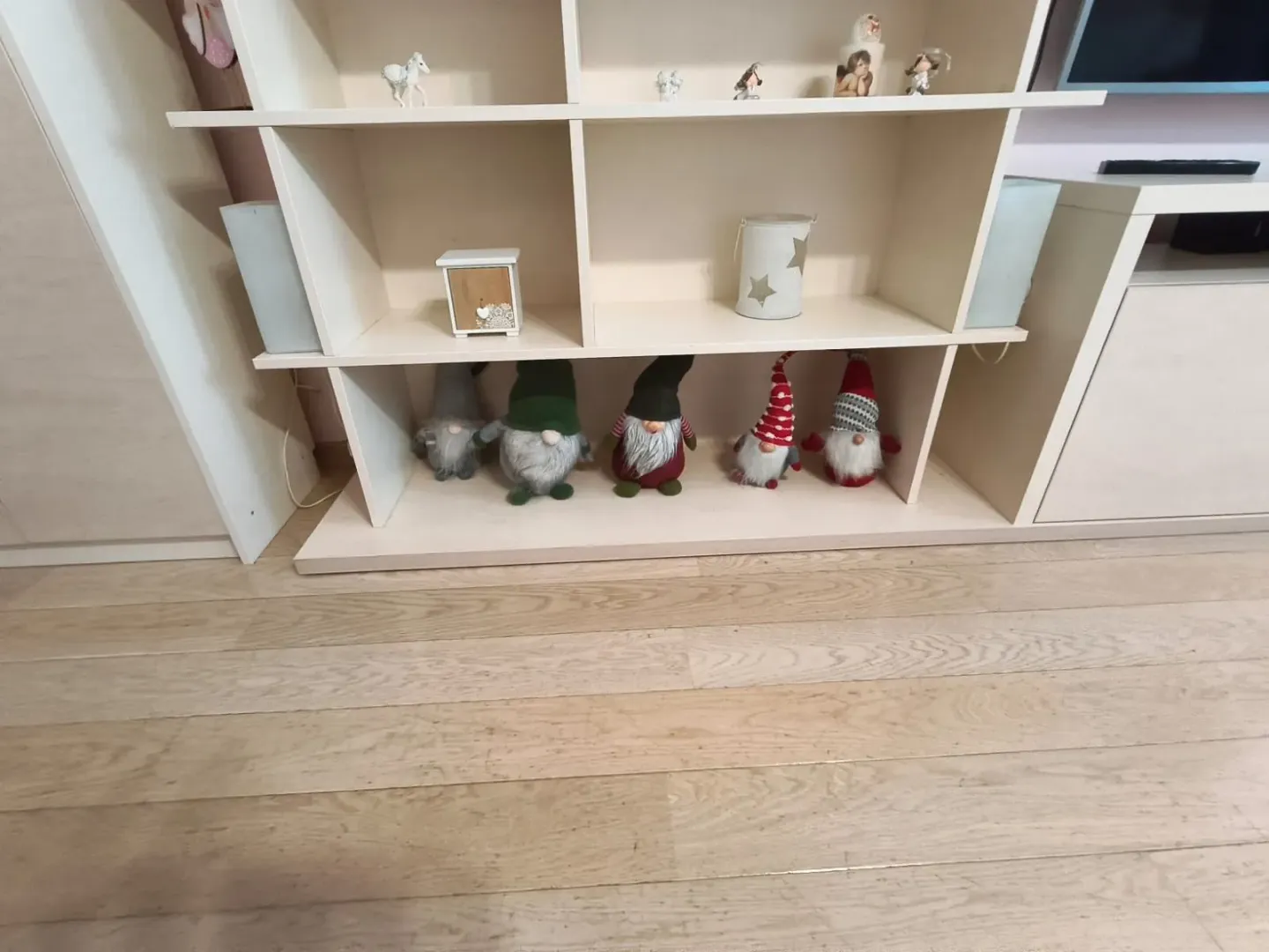 Bijela polica za knjige sa ukrasnim figurama i drvenim podom.