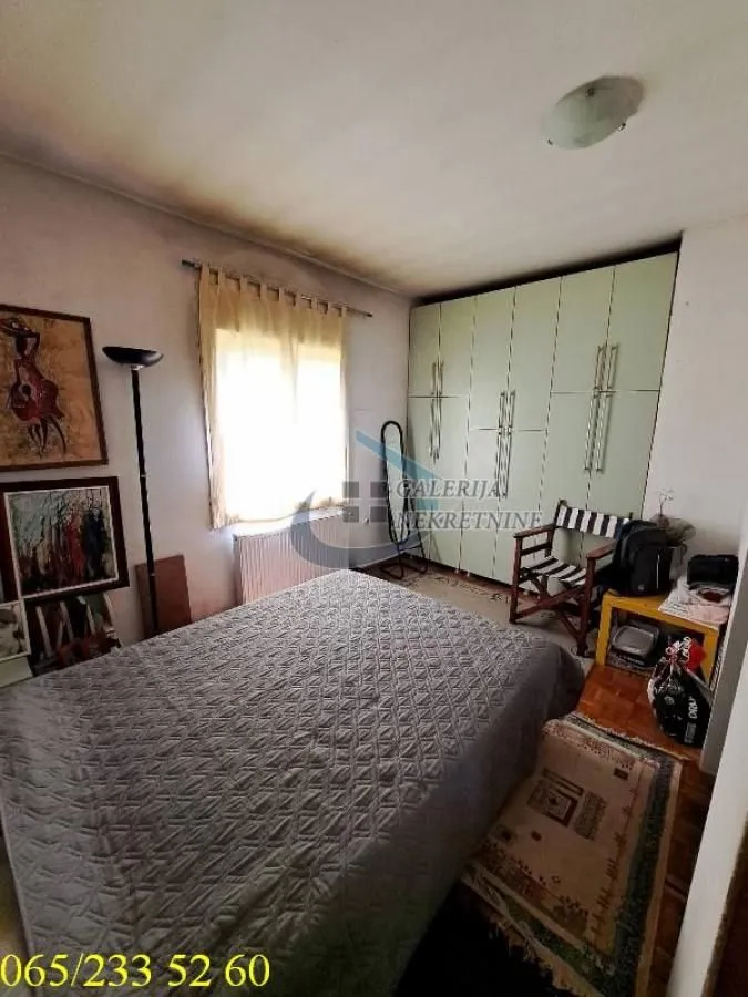 Nameštena spavaća soba sa bračnim krevetom, garderoberom i slikama na zidu.