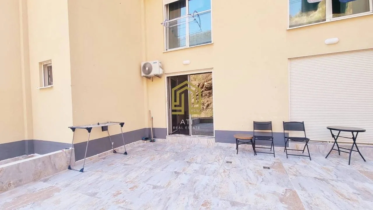 Popločano dvorište ispred žute stambene zgrade sa stolovima, stolicama i sušilicom za veš.