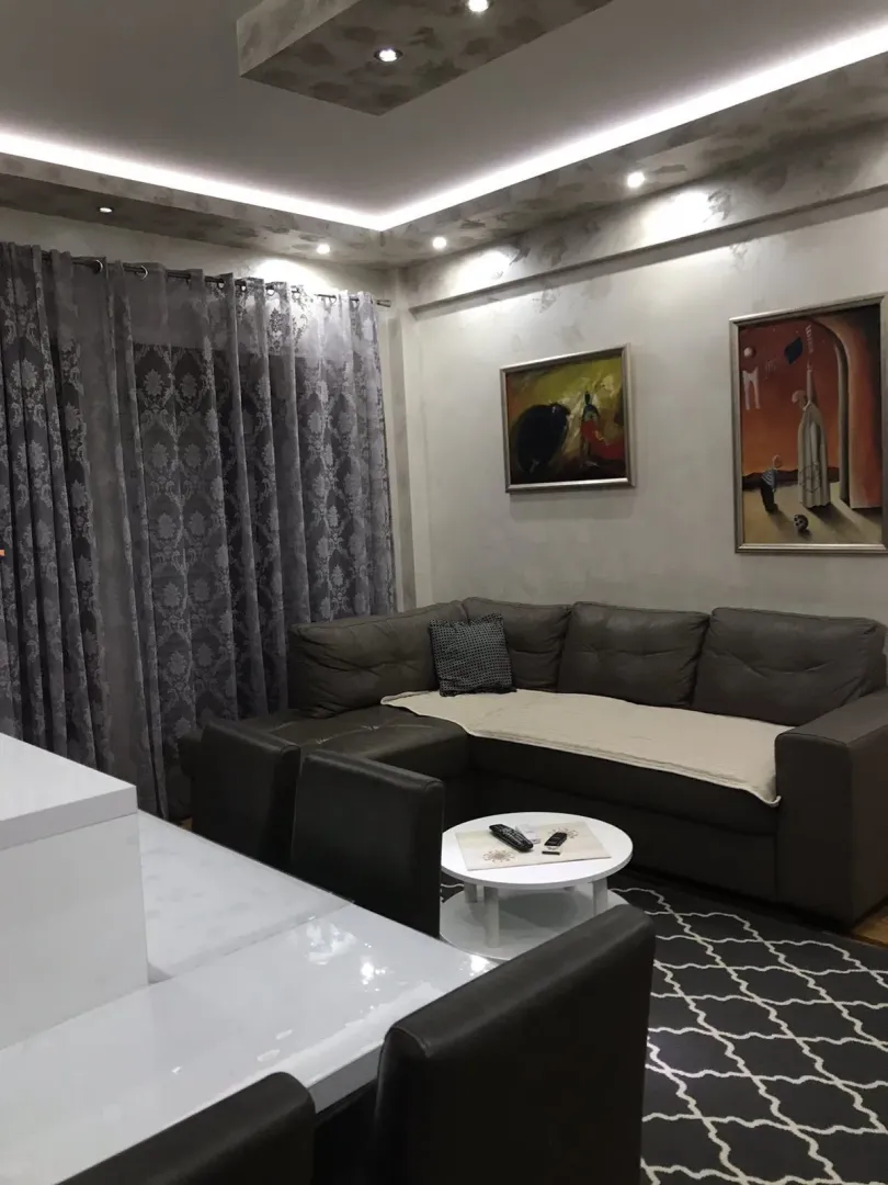 A living room with a corner sofa, art paintings on the wall, and a coffee table.