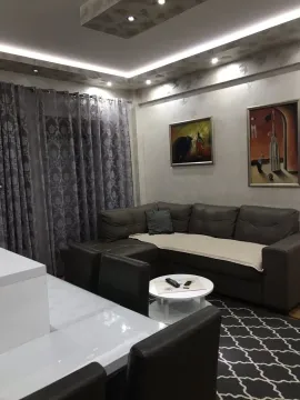 A living room with a corner sofa, art paintings on the wall, and a coffee table. - image 15