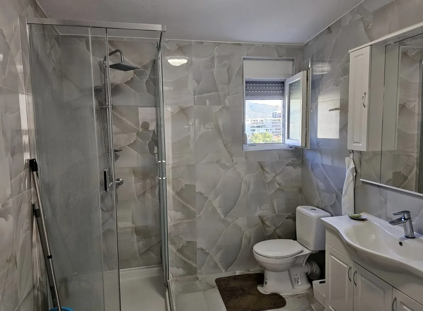 Bathroom equipped with a walk-in shower, washbasin, and toilet, featuring a window.
