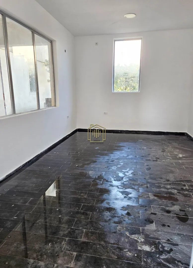 Empty unfurnished room with white walls and dark floor tiles.