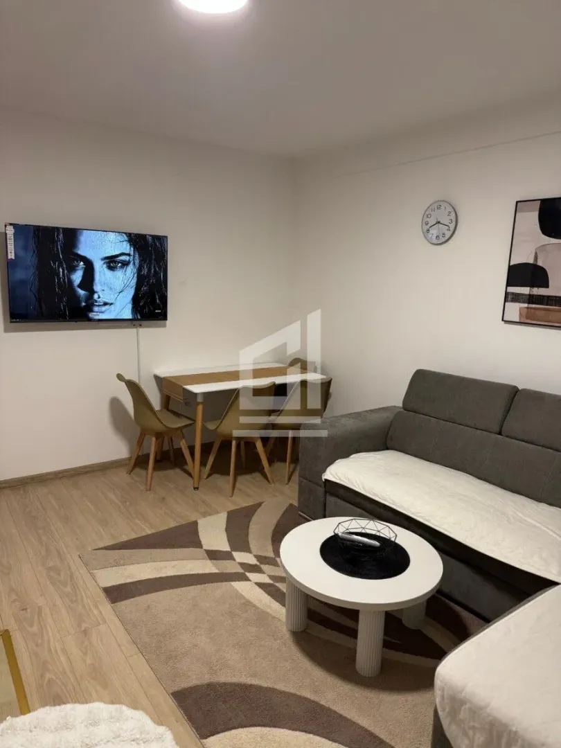 Dnevna soba sa garniturom, TV-om i trpezarijskim stolom.