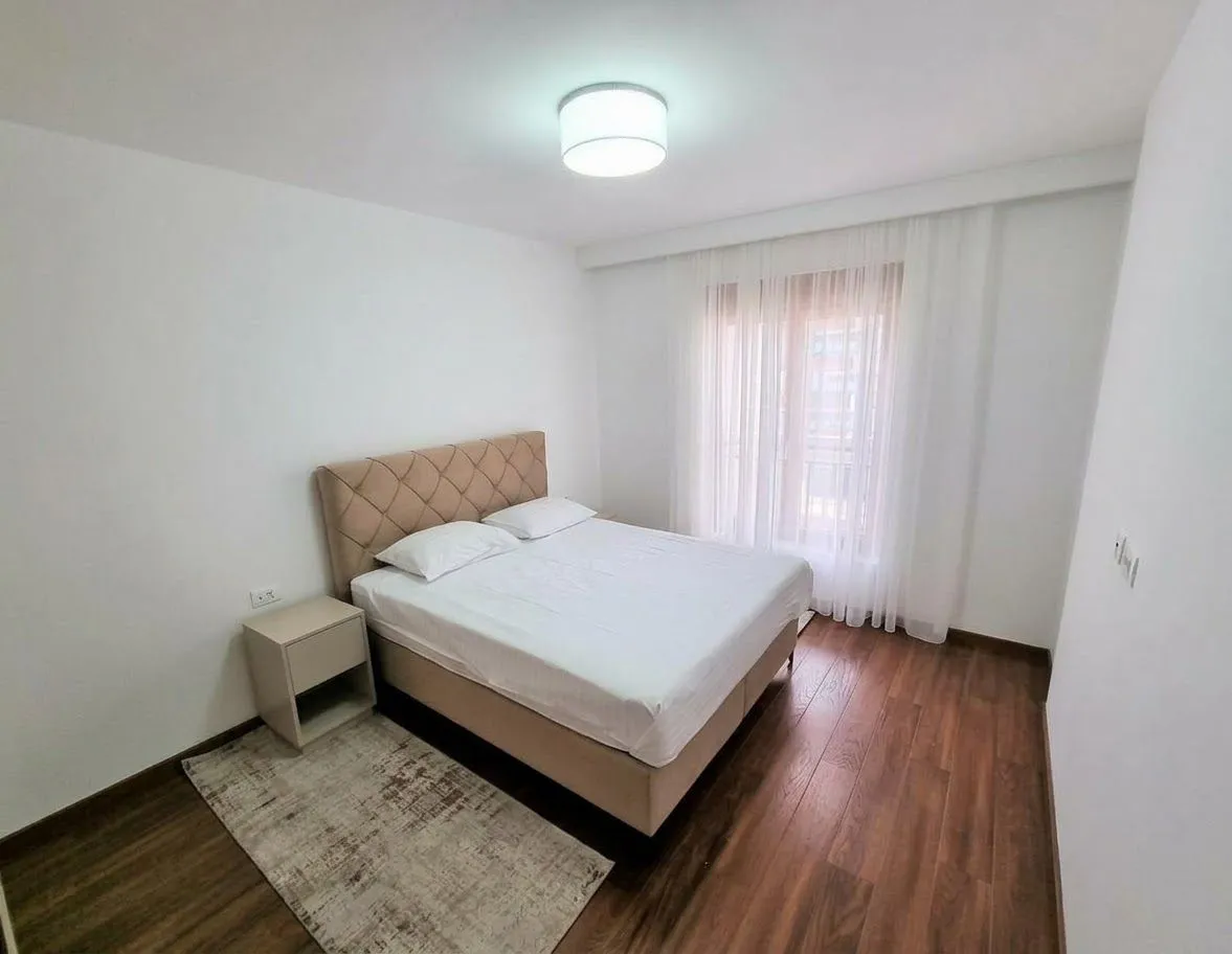 Bright bedroom with a double bed, nightstand, and window with curtains.