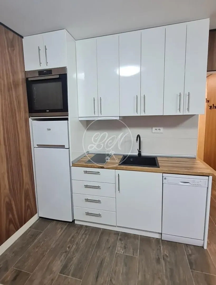 Small kitchen with white cabinets, built-in appliances and a wooden countertop.