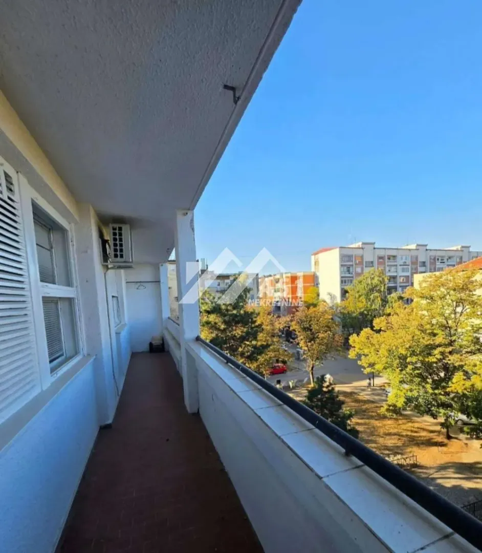 Dugi natkriveni balkon sa pogledom na ulicu i zelenilo.