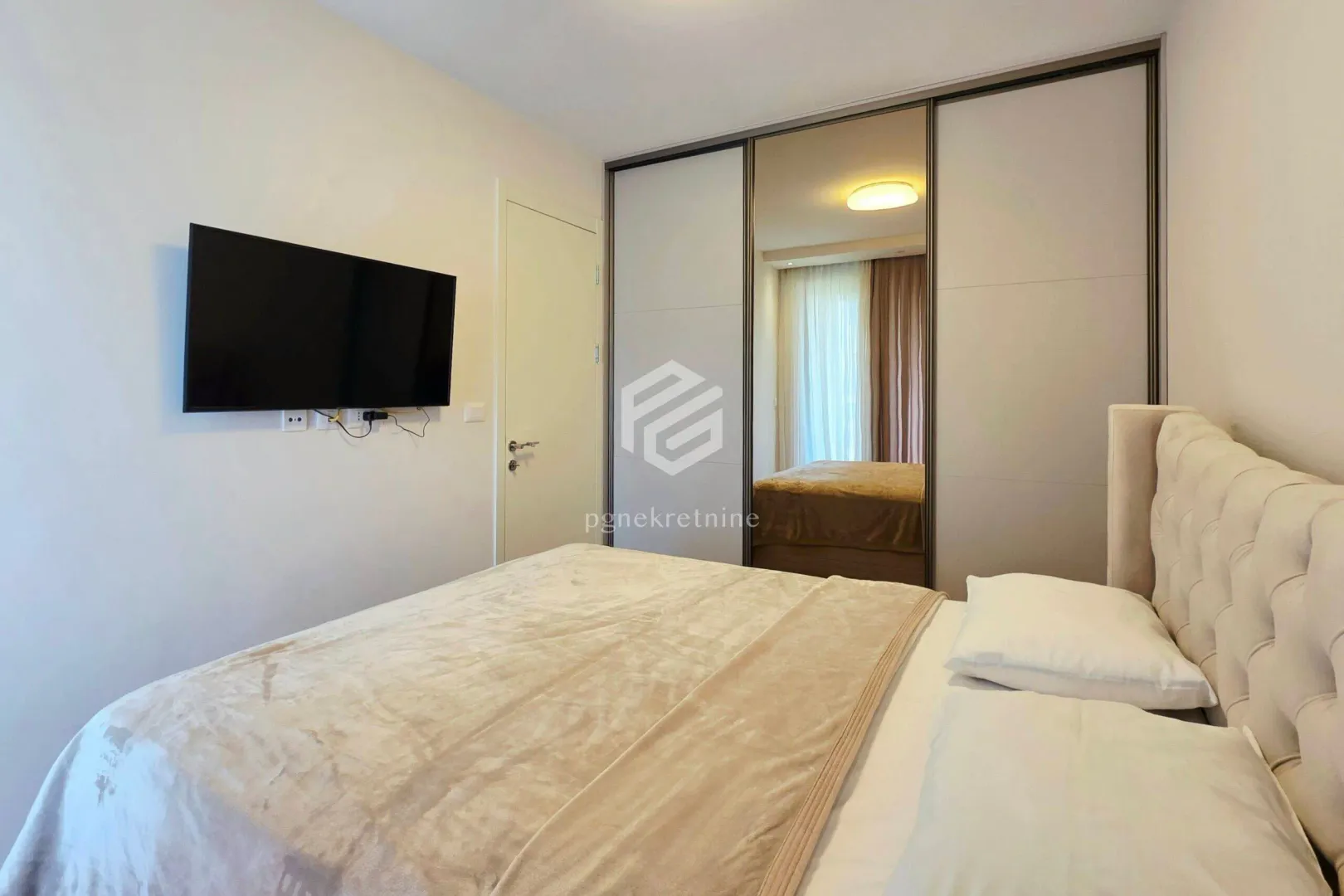 Furnished bedroom with a double bed, large wardrobe, and wall-mounted TV.