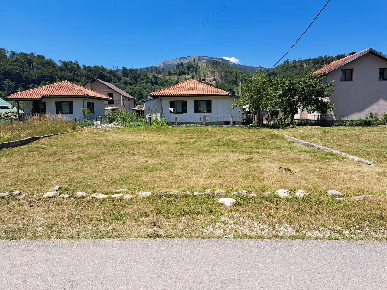 Travnati plac sa kućama u pozadini i pogledom na planinu.