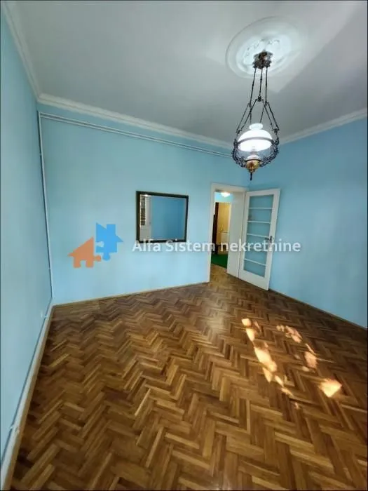 Empty room with light walls, wooden parquet flooring, and a hanging lamp.