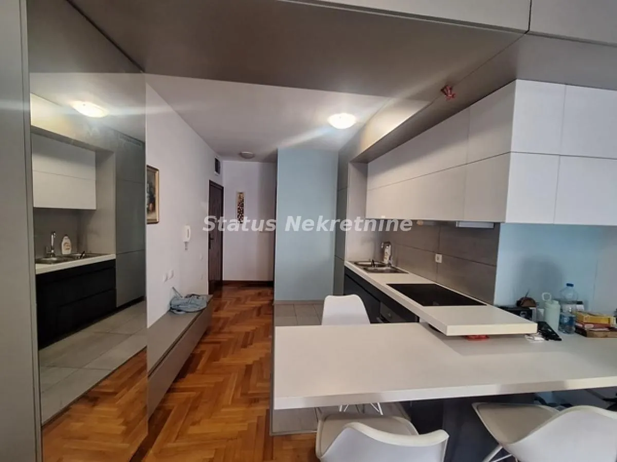 Moderna kuhinja sa šankom i trpezarijskim stolom, povezana sa hodnikom.