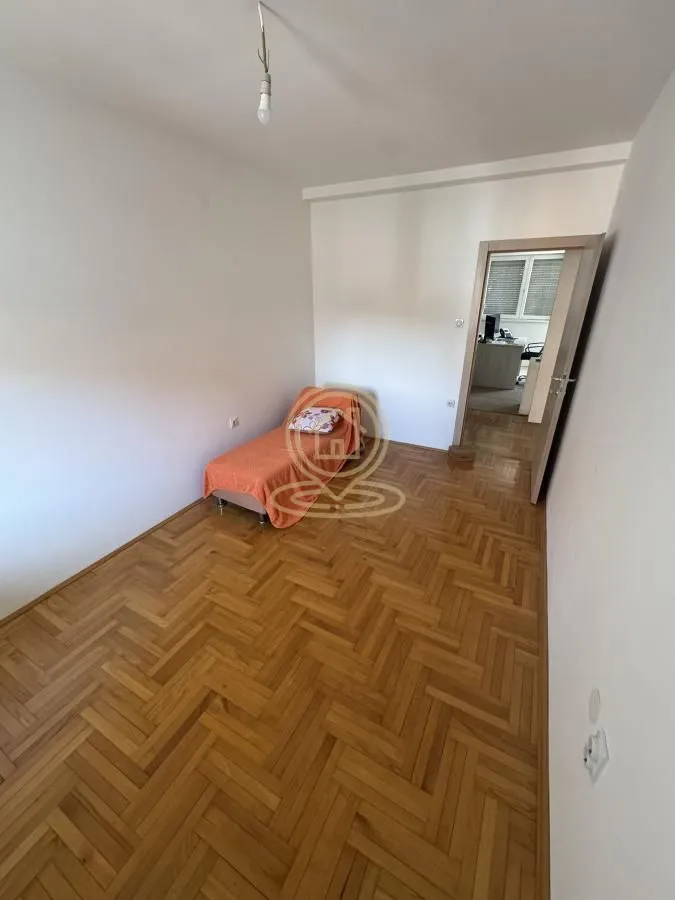 Prazna soba sa parketom i jednim krevetom.