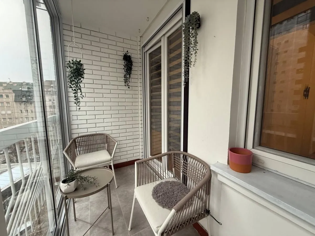 Zastakljeni balkon sa garniturom za sedenje i dekorativnim biljkama.