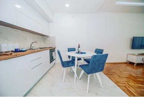 Modern kitchen with white units and a dining table with blue chairs. - image 3