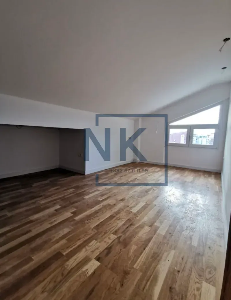 Empty attic room with hardwood flooring and sloping ceiling.