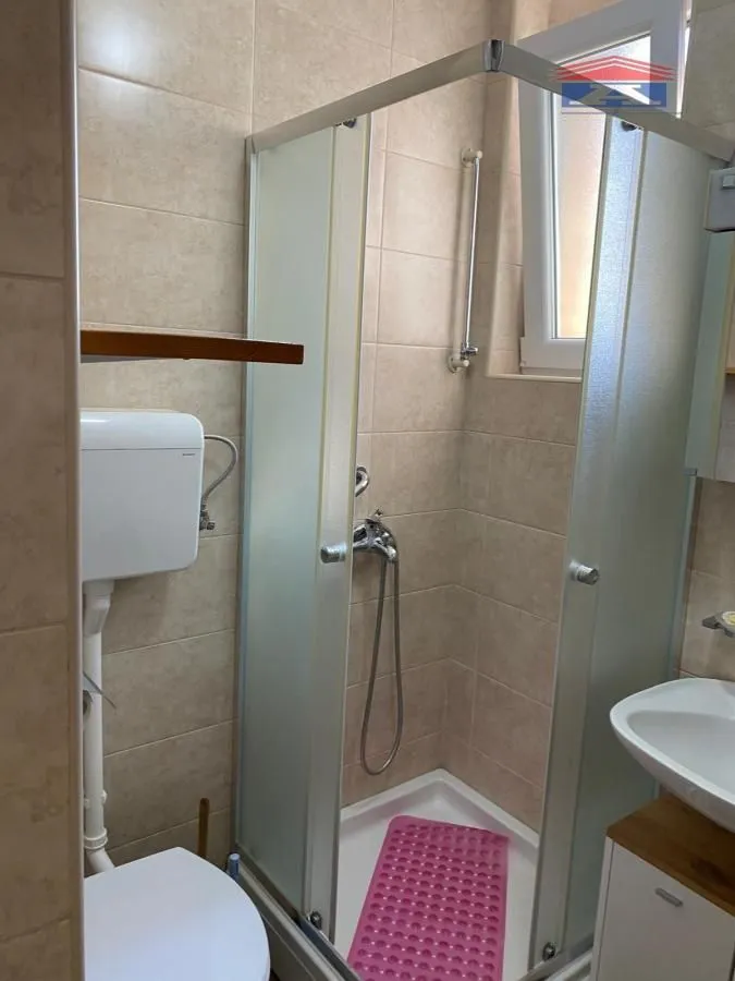 Manje kupatilo sa tuš kabinom, umivaonikom i wc šoljom obloženo keramičkim pločicama.