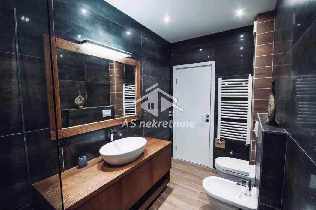 Modern bathroom with a vanity, toilet, bidet, and dark tiles.