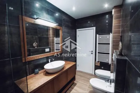 Modern bathroom with a vanity, toilet, bidet, and dark tiles. - image 10