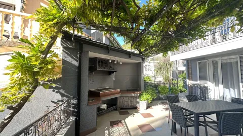A paved patio featuring an outdoor kitchen, barbecue, and dining set under a vine-covered pergola. - image 18