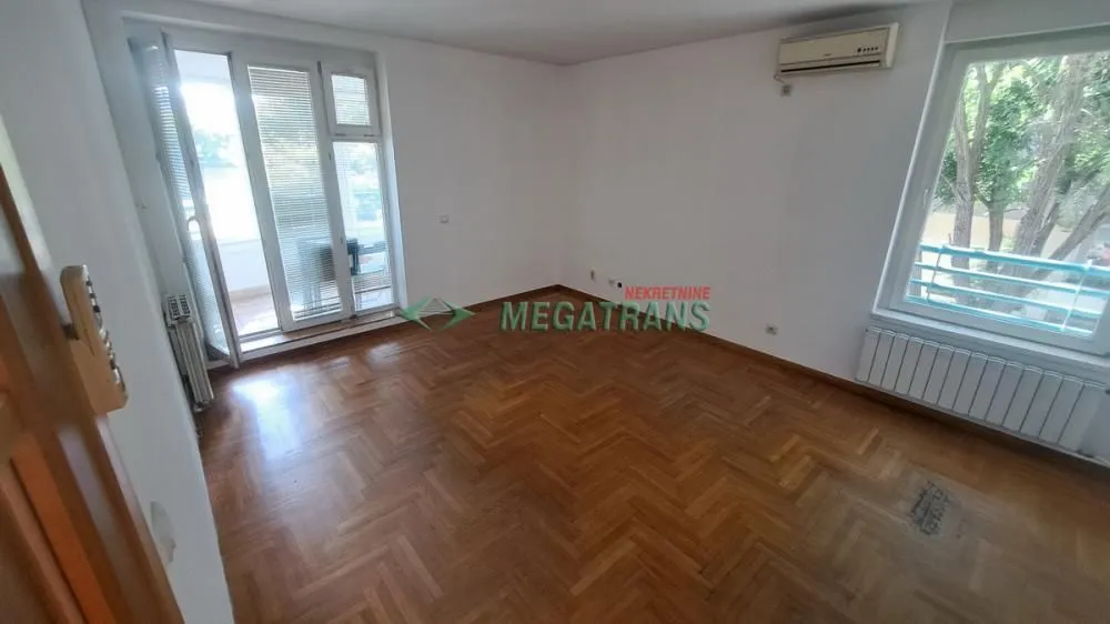 Prazna soba sa parketom, prozorima i izlazom na terasu.