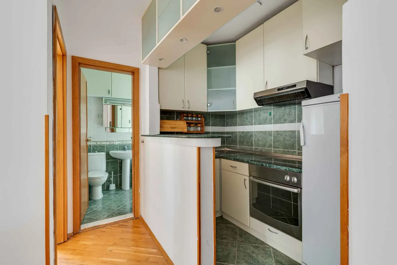 Small kitchen with a breakfast bar and built-in appliances, with a view of the bathroom in the background.