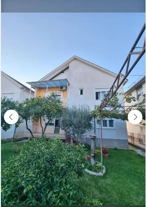 Fasada porodične kuće sa uređenim dvorištem i zelenilom.