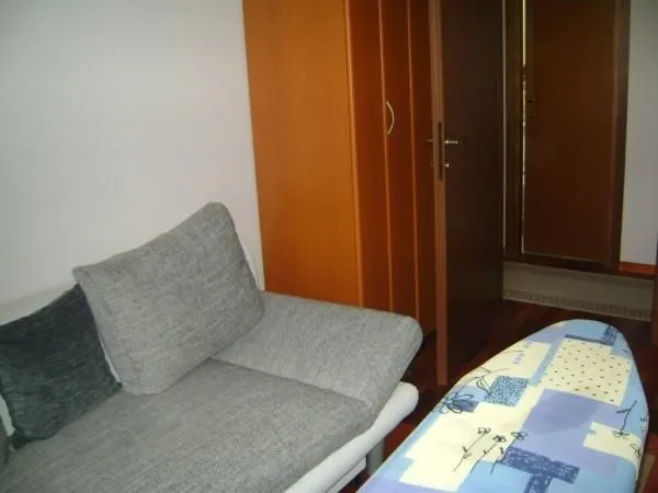 Mala soba sa kaučem, drvenim ormarom i otvorenim vratima prema hodniku.