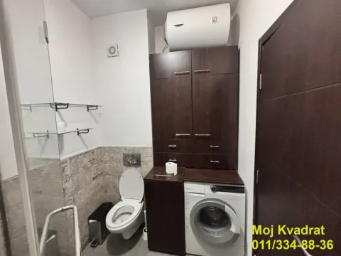 Manje kupatilo sa wc šoljom, veš mašinom i tamnim drvenim ormarićem. - image 10