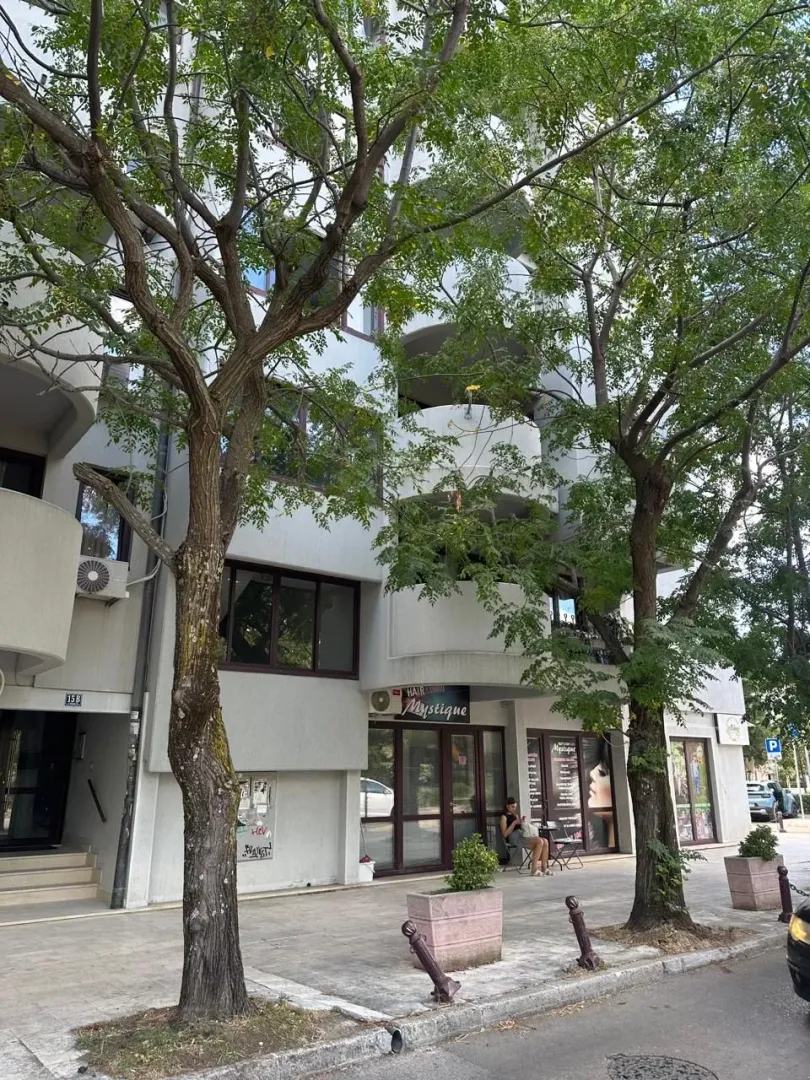 Exterior of a residential building with a ground-floor commercial space and trees in front.