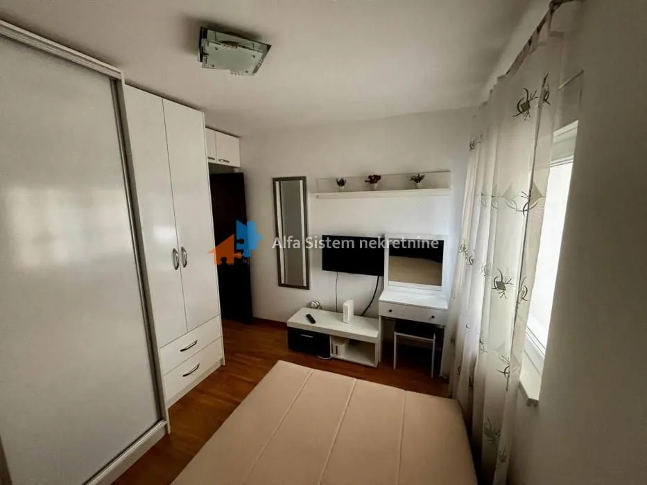 Nameštena spavaća soba sa krevetom, garderoberom i televizorom.
