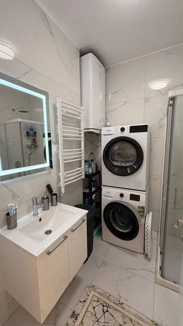 Modernly equipped bathroom with a washbasin, shower cabin, and laundry machines.