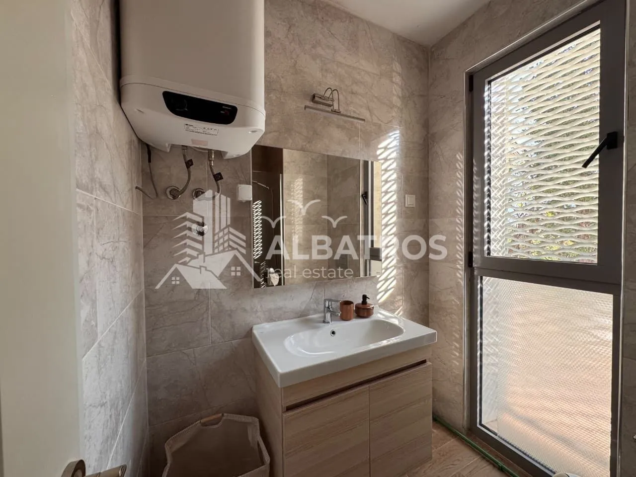 Smaller bathroom with a washbasin, mirror, water heater, and a window.