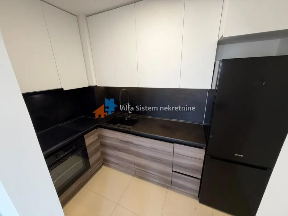 Small modern kitchen with white and wooden cabinets and a black refrigerator.