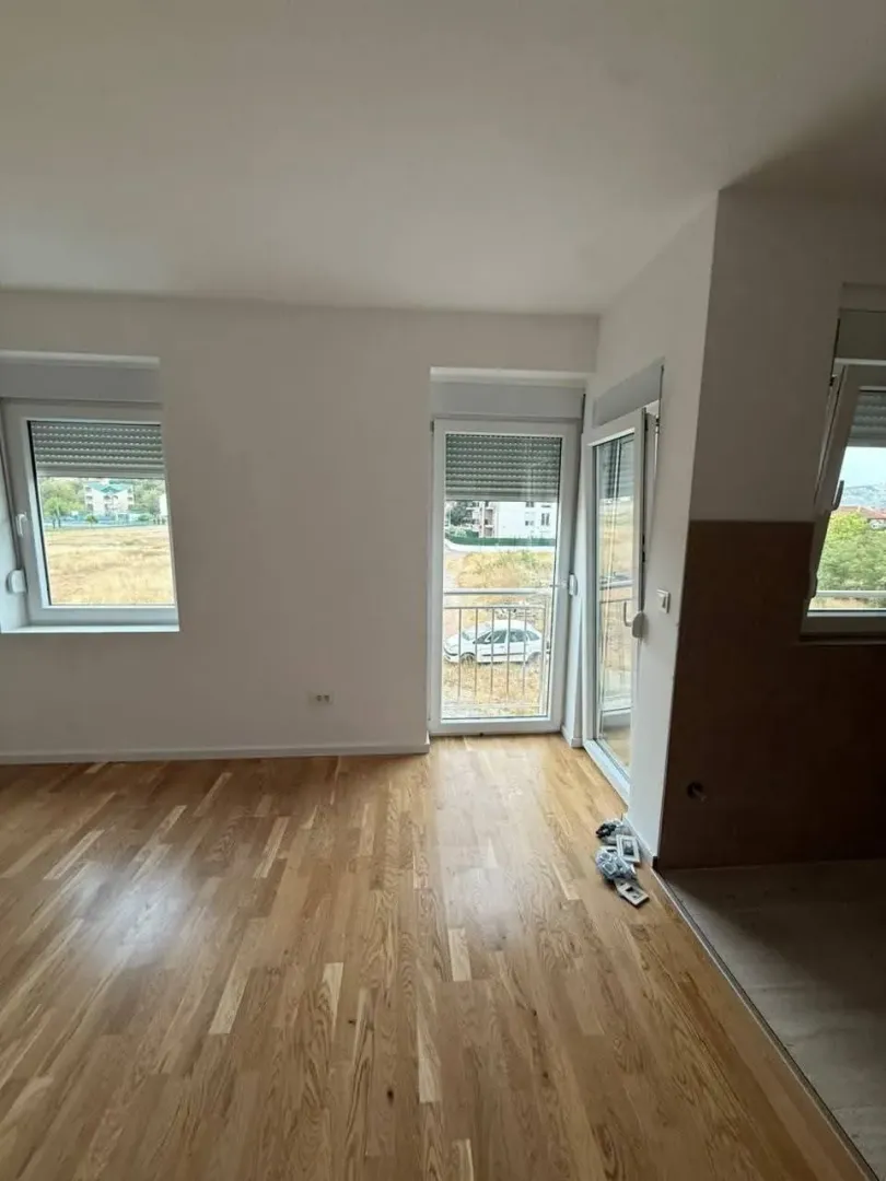 Prazna prostorija sa drvenim podom i izlazom na terasu.
