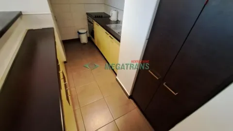 Pogled na usku kuhinju sa žutim elementima i tamnim ormarima. - image 7