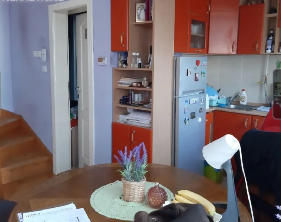 Kuhinja sa trpezarijskim stolom i narandžastim kuhinjskim elementima.