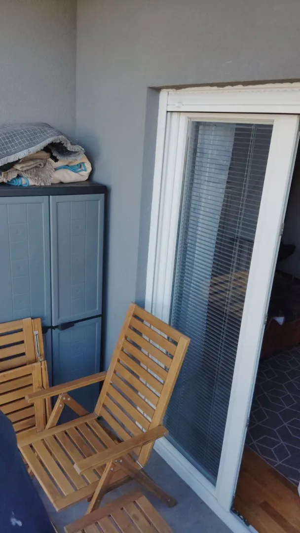 Balkon sa drvenim stolicama i plastičnim ormarom pored balkonskih vrata.
