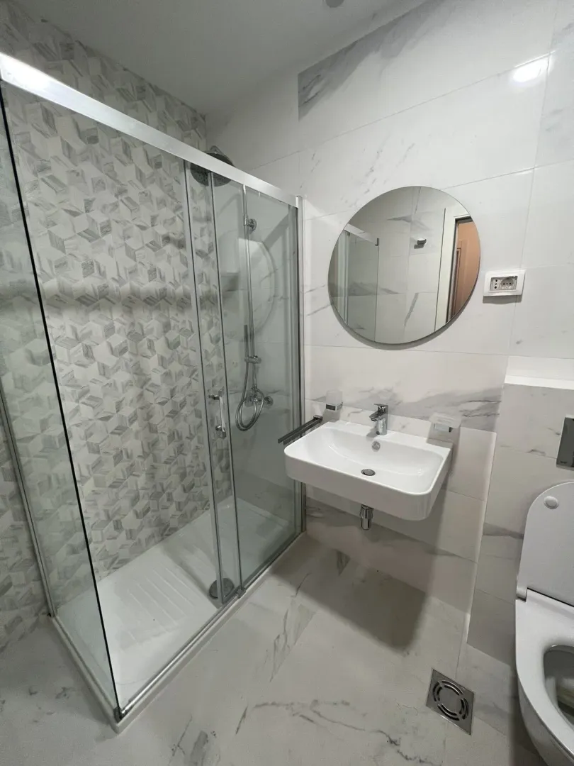 Modern bathroom with a shower cabin and a round mirror.