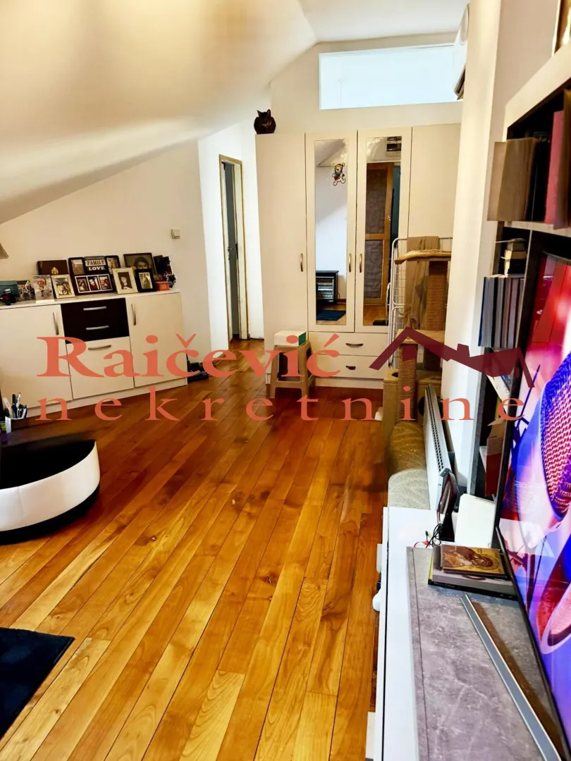 Attic living room with wooden flooring, a wardrobe, and a TV.