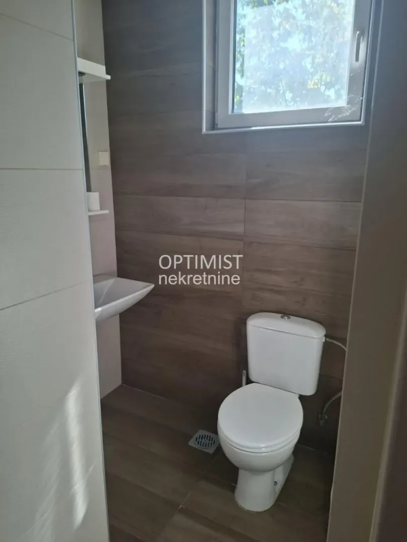 Manje kupatilo sa WC šoljom, umivaonikom i prozorom.