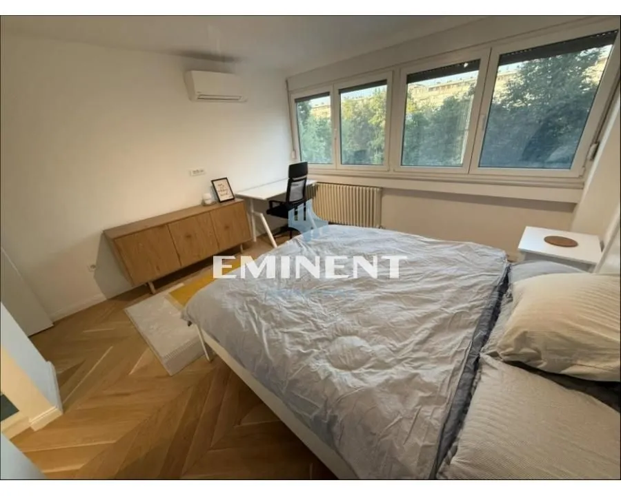 Furnished bedroom with a double bed, desk, and large windows.