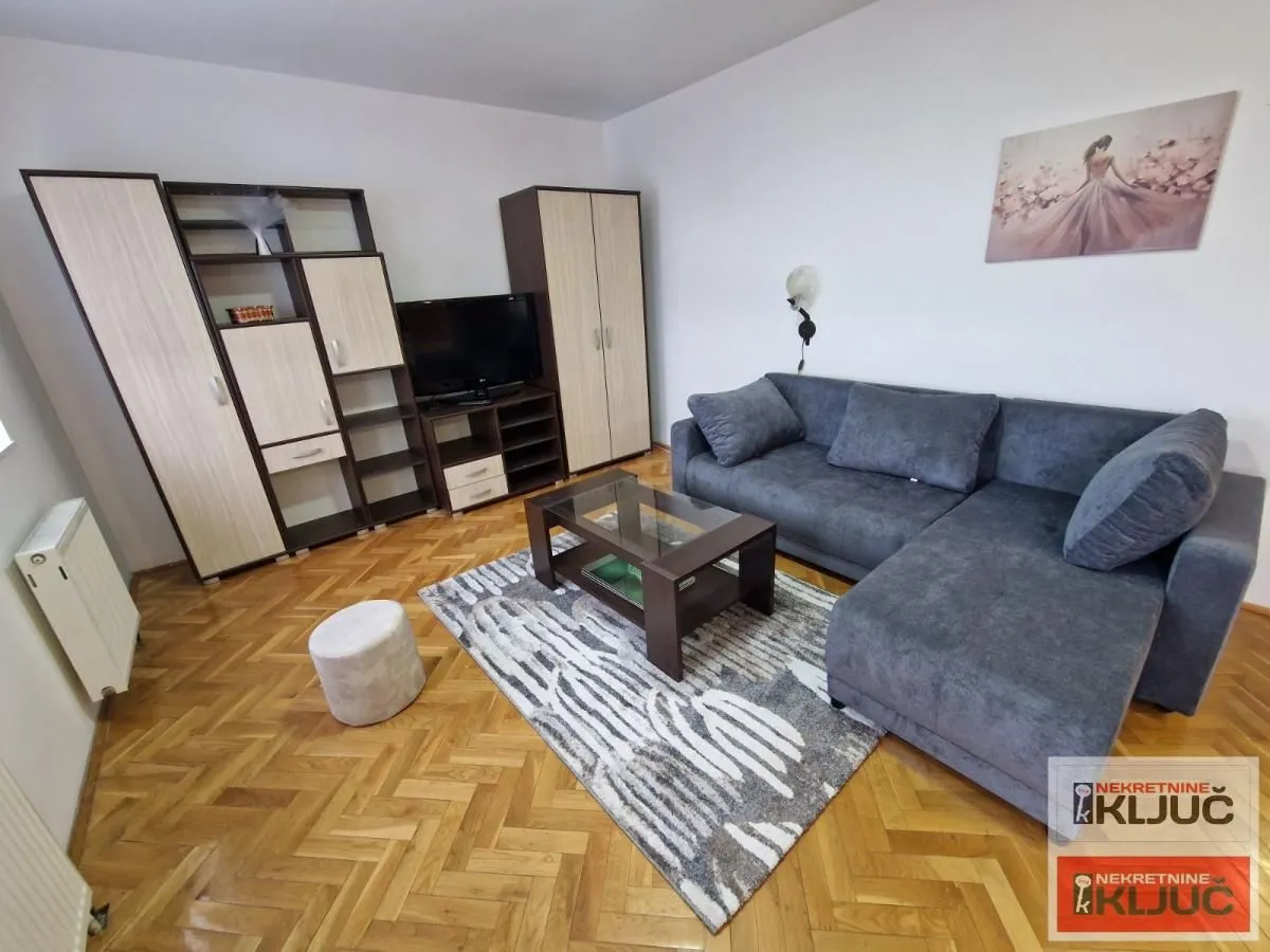 Dnevna soba sa garniturom, televizorom i drvenim nameštajem.