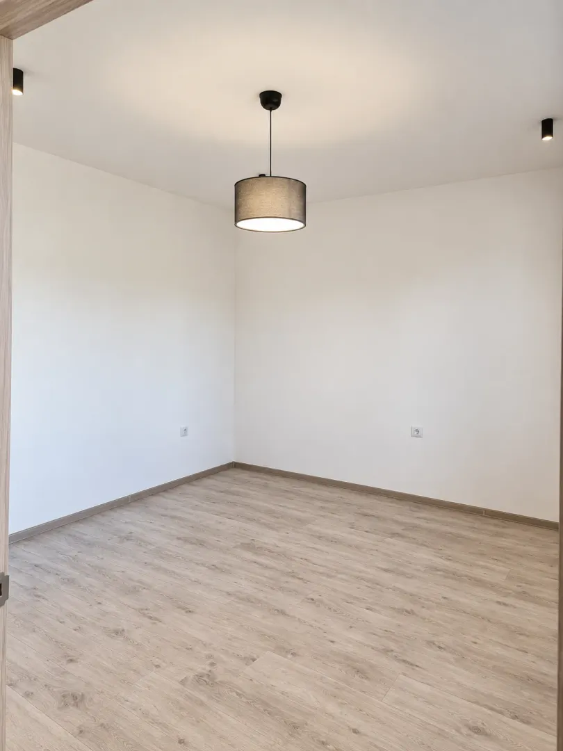 Empty room with white walls, wooden flooring, and a pendant lamp.